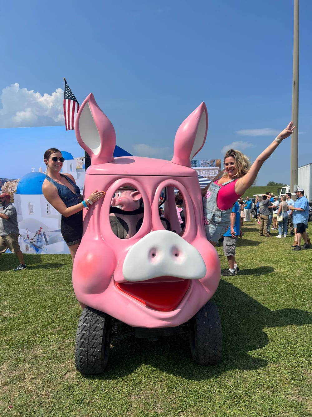 Carla with her arm in the air next to a giant pink pig cart at Hogs for the Cause