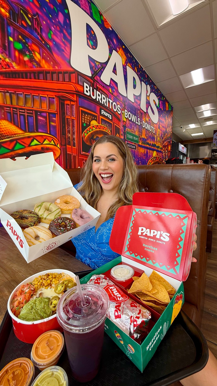 Carla at Papi's with donuts, a burrito bowl and a combo box in front of the Papi's mural